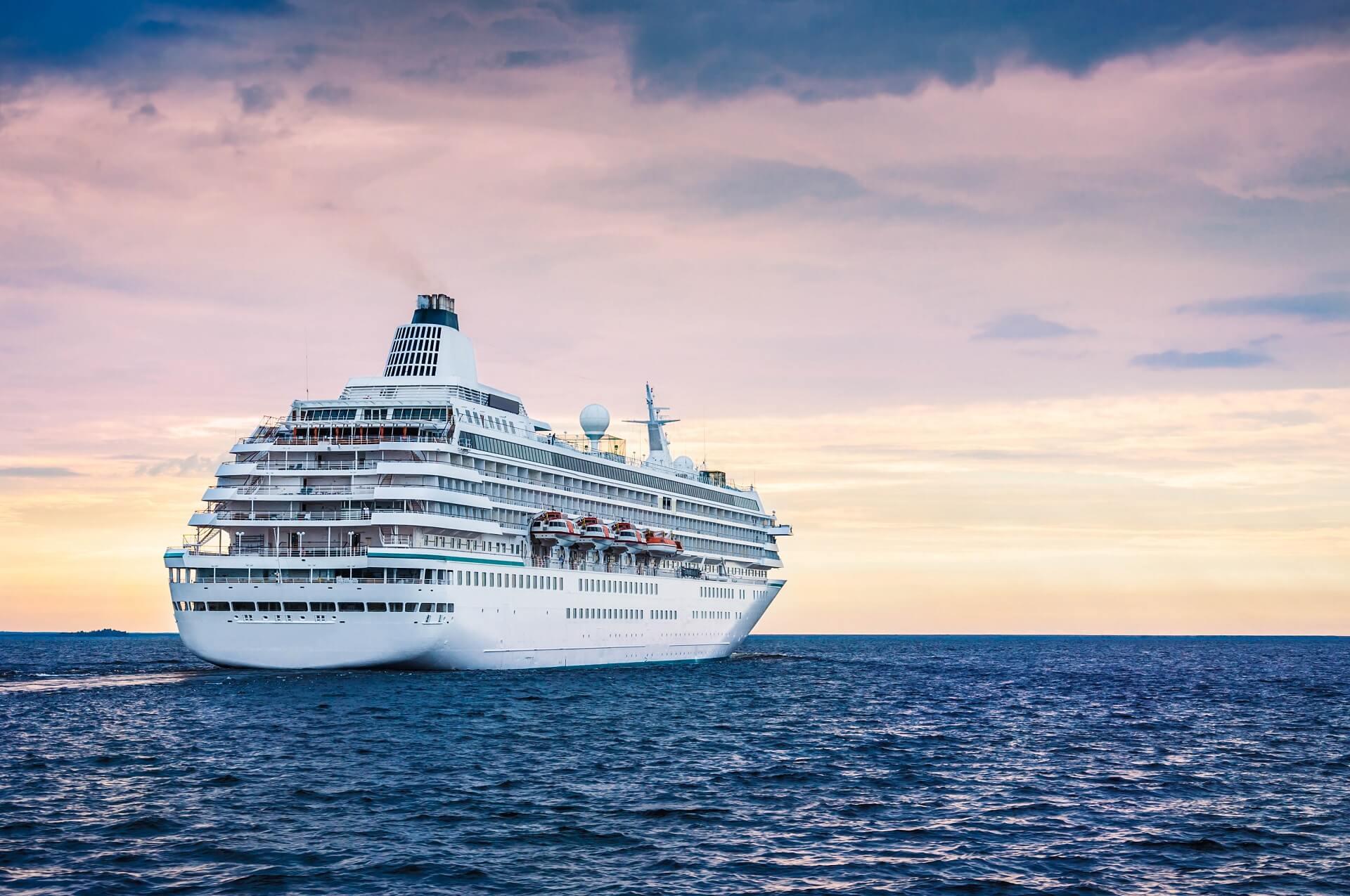 A large white cruise ship sails before a softly colored sunset on the North Sea. Popular cruise routes lead here to destinations like the Norwegian fjords or the Lofoten.